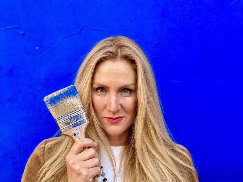 Virginie Georgeault, pinceau à la main, devant un mur enduit bleu outremer